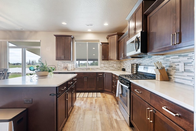 kitchen with stainless steel appliances, light wood-style flooring, a sink, light countertops, and tasteful backsplash