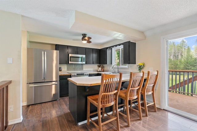 kitchen featuring stainless steel appliances, dark cabinetry, light countertops, dark wood-type flooring, and a textured ceiling