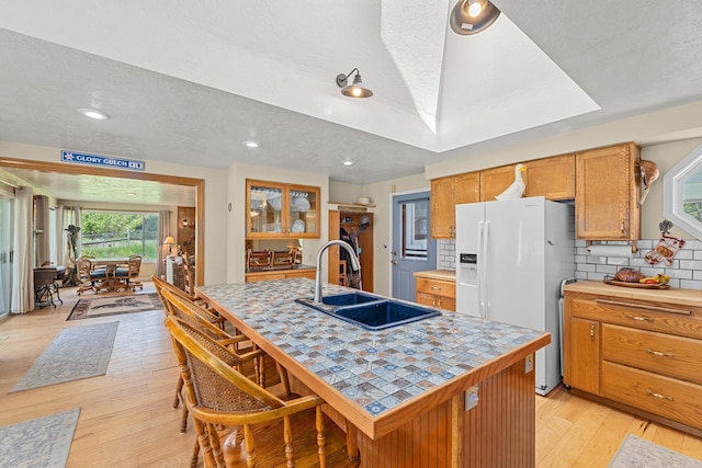2443 Flowery Trail Rd, Usk, WA 99180 - kitchen featuring white refrigerator with ice dispenser, a sink, light wood-style floors, decorative backsplash, and a center island with sink