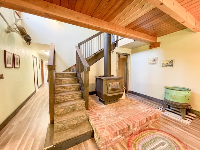 stairs featuring beamed ceiling, wood finished floors, baseboards, wooden ceiling, and a wood stove