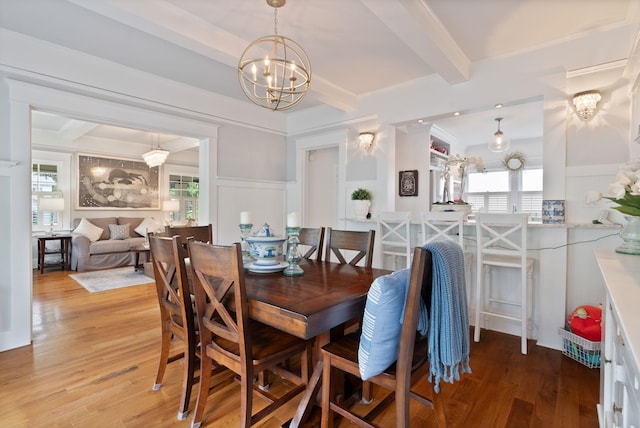 dining space featuring a chandelier, a decorative wall, beamed ceiling, plenty of natural light, and light wood-type flooring