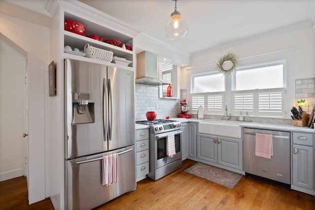 kitchen with stainless steel appliances, wall chimney exhaust hood, gray cabinets, a sink, and tasteful backsplash