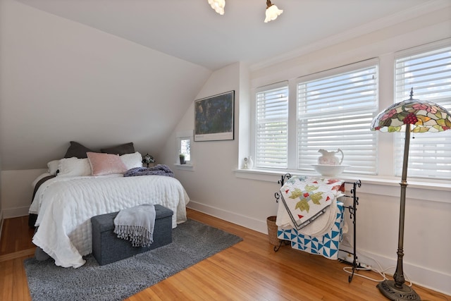 bedroom with vaulted ceiling, wood finished floors, and baseboards