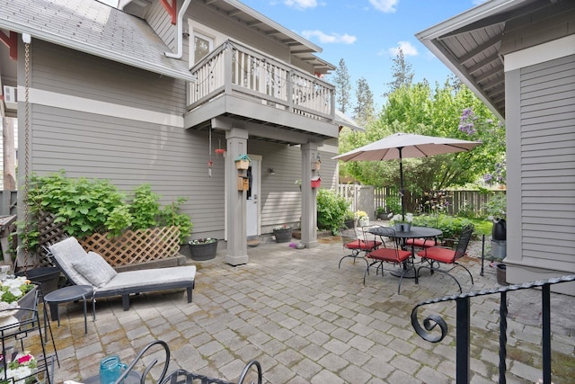 view of patio featuring outdoor dining space, fence, and a balcony