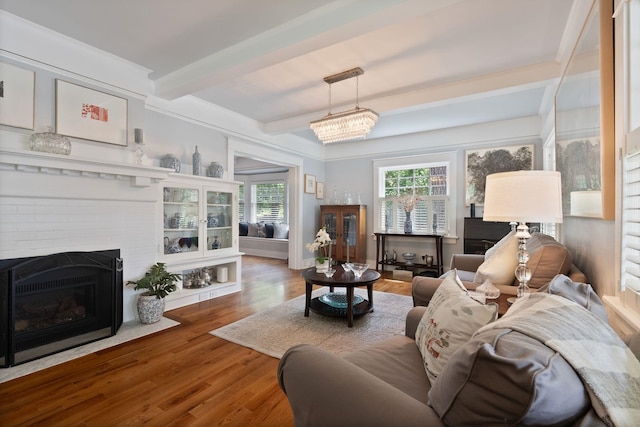 living area with beamed ceiling, wood finished floors, and a brick fireplace