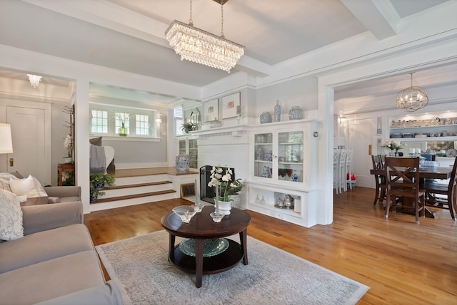 living area with a chandelier, light wood-style flooring, beamed ceiling, and crown molding