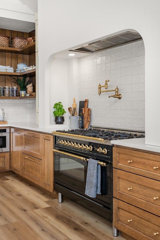 23114 W Mcfarlane Rd, Medical Lake, WA 99022 - kitchen with high end black range, decorative backsplash, stainless steel oven, brown cabinets, and light wood-style flooring