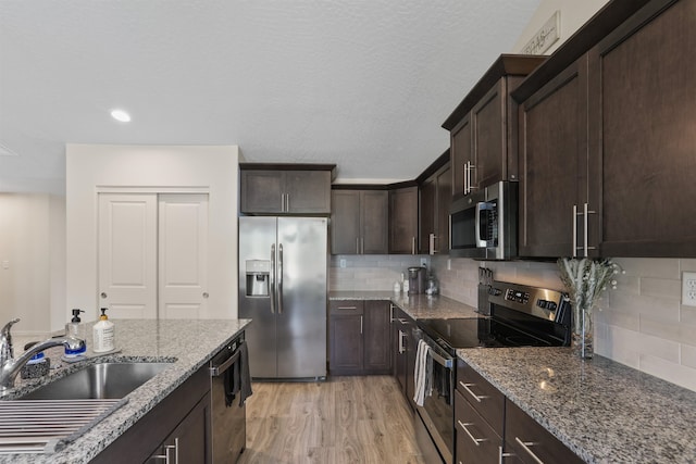 8604 W 8th Ave, Spokane, WA 99224 - kitchen featuring appliances with stainless steel finishes, a sink, stone countertops, dark brown cabinetry, and light wood-style floors