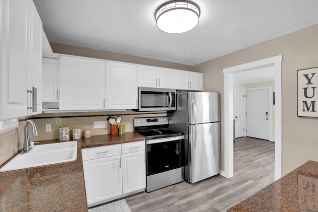 1419 E Glass Ave, Spokane, WA 99207 - kitchen with stainless steel appliances, a sink, light wood finished floors, white cabinets, and a textured ceiling