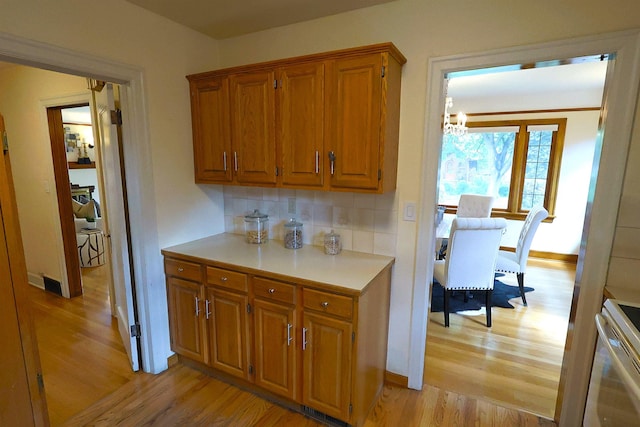 417 W 26th Ave, Spokane, WA 99203 - kitchen featuring light wood finished floors, brown cabinetry, backsplash, light countertops, and a chandelier
