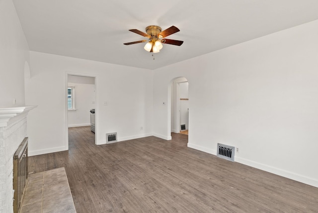 3215 W Longfellow Ave, Spokane, WA 99205 - unfurnished living room featuring arched walkways, a ceiling fan, wood finished floors, a fireplace, and baseboards