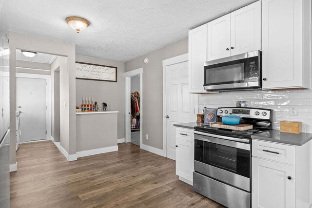 4824 N Stone St, Spokane, WA 99207 - kitchen with stainless steel appliances, wood finished floors, decorative backsplash, dark countertops, and white cabinetry