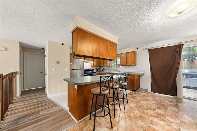 3712 E 12th Ave, Spokane, WA 99202 - kitchen featuring stainless steel appliances, brown cabinets, a textured ceiling, under cabinet range hood, and a breakfast bar area