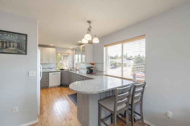 4701 E 13th Ave, Spokane Valley, WA 99212 - kitchen featuring white dishwasher, a peninsula, decorative backsplash, a kitchen bar, and light stone counters