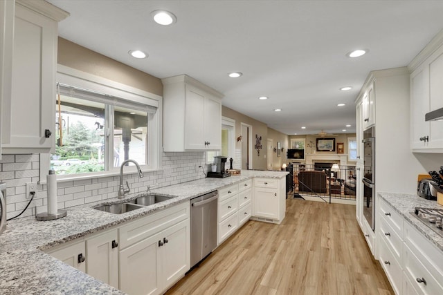 4921 W Londale Ct, Spokane, WA 99208 - kitchen with stainless steel appliances, a sink, a fireplace, white cabinetry, and decorative backsplash