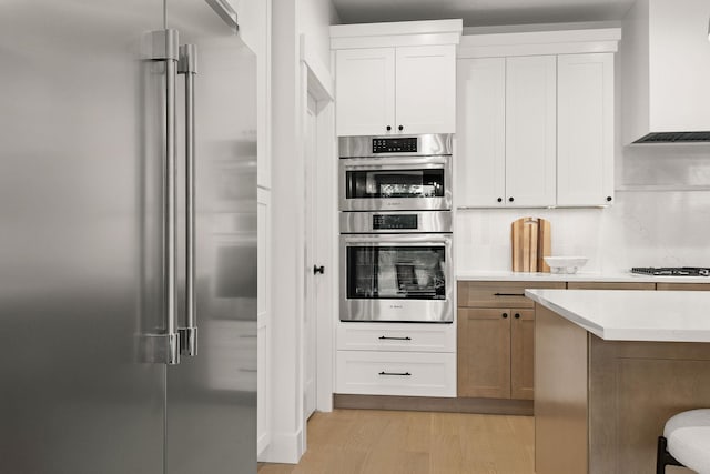 11711 E Honeycomb Springs Ln, Spokane, WA 99206 - kitchen featuring appliances with stainless steel finishes, wall chimney exhaust hood, light wood finished floors, light countertops, and white cabinets