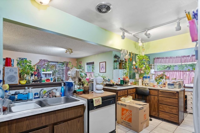 2029 E Sharp Ave, Spokane, WA 99202 - kitchen featuring white dishwasher, light tile patterned floors, light countertops, a sink, and brown cabinetry