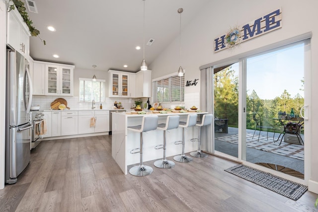 5475 Peggy Way, Deer Park, WA 99006 - kitchen featuring appliances with stainless steel finishes, light wood-style floors, tasteful backsplash, a breakfast bar area, and glass insert cabinets