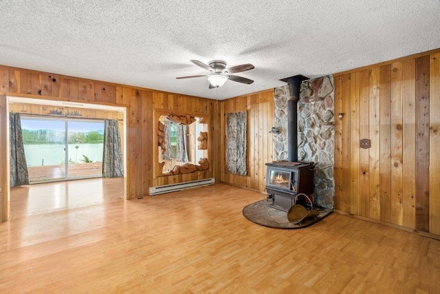 472 Snow Berry Ln, Usk, WA 99180 - unfurnished living room with a wood stove, wood walls, baseboard heating, ceiling fan, and a textured ceiling