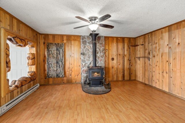 472 Snow Berry Ln, Usk, WA 99180 - unfurnished living room featuring a baseboard heating unit, wood finished floors, a wood stove, wooden walls, and a textured ceiling
