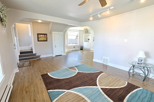 1327 N Howard St, Spokane, WA 99201 - unfurnished living room featuring a baseboard heating unit, arched walkways, wood finished floors, and a ceiling fan