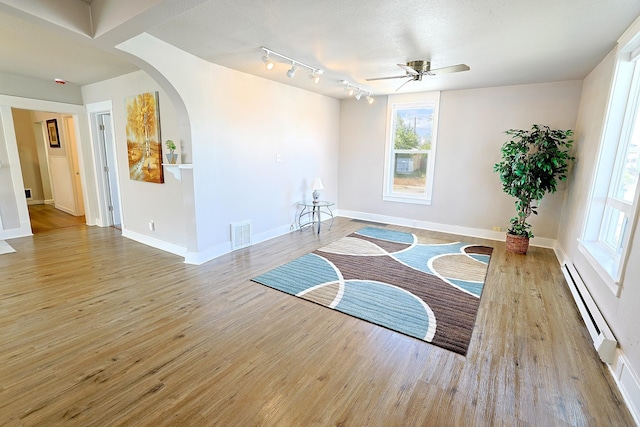 1327 N Howard St, Spokane, WA 99201 - unfurnished room featuring a baseboard radiator, arched walkways, wood finished floors, a ceiling fan, and baseboards