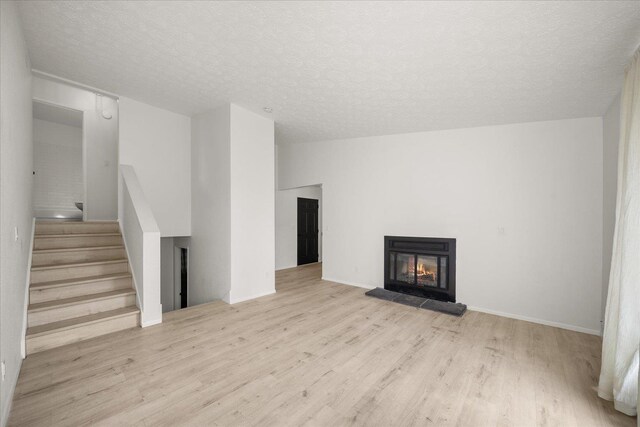 20716 E Gilbert Rd, Otis Orchards, WA 99027 - unfurnished living room with wood finished floors, a textured ceiling, a glass covered fireplace, and stairs
