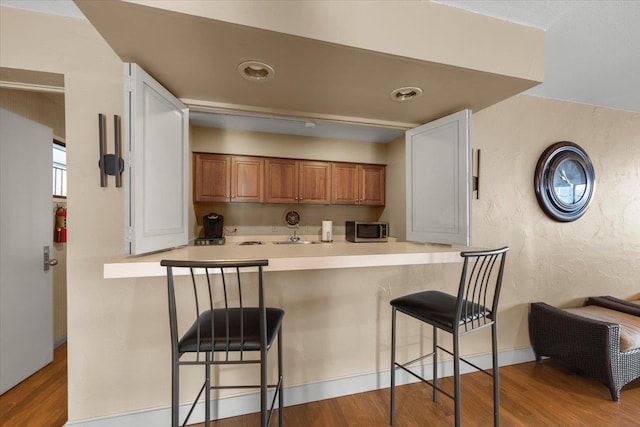 700 W 7th Ave # 206, Spokane, WA 99204 - kitchen with stainless steel microwave, brown cabinetry, wood finished floors, a kitchen breakfast bar, and a peninsula