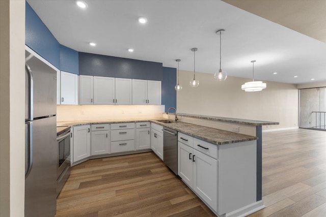 700 W 7th Ave # 206, Spokane, WA 99204 - kitchen with stainless steel appliances, a peninsula, a sink, wood finished floors, and white cabinets