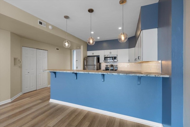 700 W 7th Ave # 206, Spokane, WA 99204 - kitchen with appliances with stainless steel finishes, a kitchen breakfast bar, a peninsula, light wood finished floors, and decorative backsplash