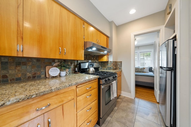 918 W 18th Ave, Spokane, WA 99203 - kitchen with under cabinet range hood, appliances with stainless steel finishes, light stone counters, light tile patterned floors, and tasteful backsplash