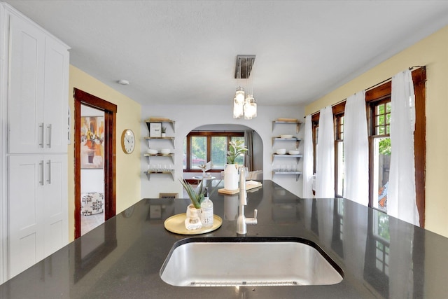 7311 E Fairview Ave, Spokane Valley, WA 99212 - kitchen with arched walkways, a sink, dark countertops, and white cabinetry