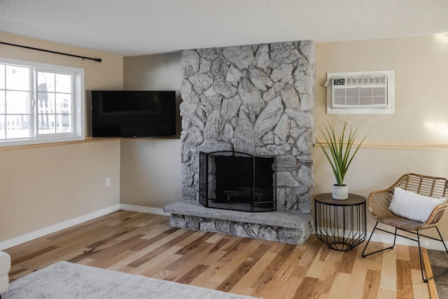 423 W Providence Ave, Spokane, WA 99205 - living room with wood finished floors, a textured ceiling, an AC wall unit, baseboards, and a stone fireplace