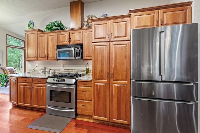 5999 E Roger Dr, Post Falls, ID 83854 - kitchen featuring stainless steel appliances, wood finished floors, light stone countertops, and brown cabinetry
