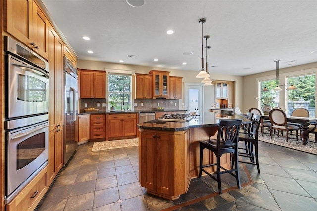 3311 E Chisholm Ln, Spokane, WA 99223 - kitchen featuring appliances with stainless steel finishes, a center island, brown cabinetry, backsplash, and glass insert cabinets