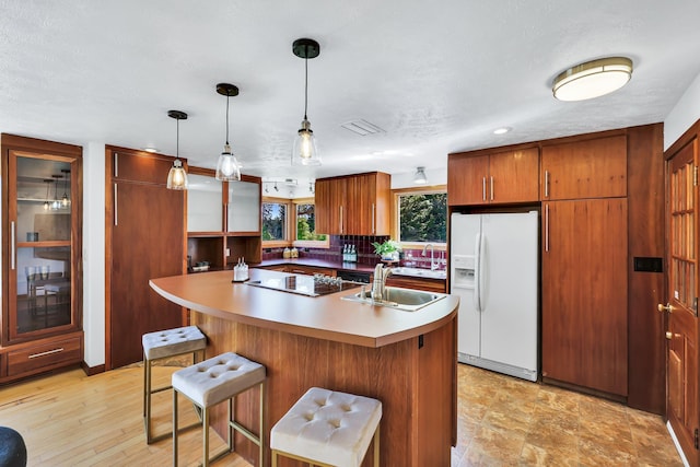10401 N College Cir, Spokane, WA 99218 - kitchen featuring white fridge with ice dispenser, a sink, black electric stovetop, backsplash, and a kitchen bar