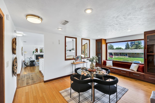 10401 N College Cir, Spokane, WA 99218 - dining room featuring light wood-style floors, a textured ceiling, a glass covered fireplace, and baseboards