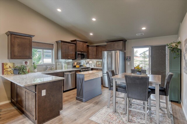 8202 W Quaking Rd, Spokane, WA 99224 - kitchen with appliances with stainless steel finishes, a peninsula, vaulted ceiling, decorative backsplash, and light stone counters