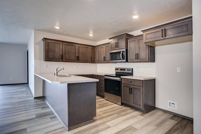 18509 E Michielli Ln, Spokane Valley, WA 99016 - kitchen with stainless steel appliances, a sink, a peninsula, dark brown cabinetry, and light wood finished floors