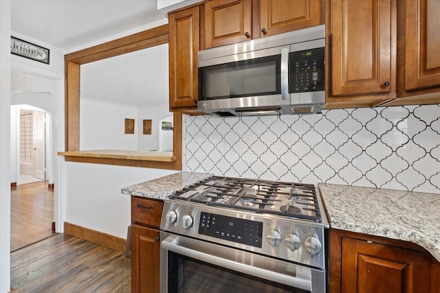 10503 E Valleyway Ave, Spokane Valley, WA 99206 - kitchen with appliances with stainless steel finishes, dark wood finished floors, decorative backsplash, and brown cabinetry