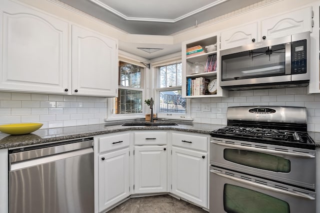 704 E 20th Ave, Spokane, WA 99203 - kitchen with stainless steel appliances, dark stone counters, white cabinetry, a sink, and ornamental molding