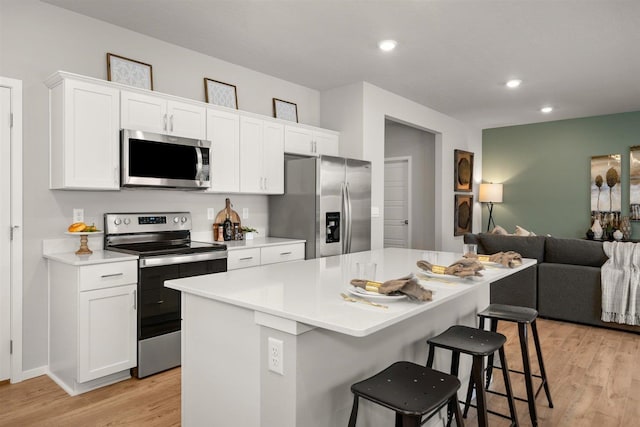 701 E K St, Deer Park, WA 99006 - kitchen featuring stainless steel appliances, light wood finished floors, open floor plan, a kitchen bar, and white cabinetry
