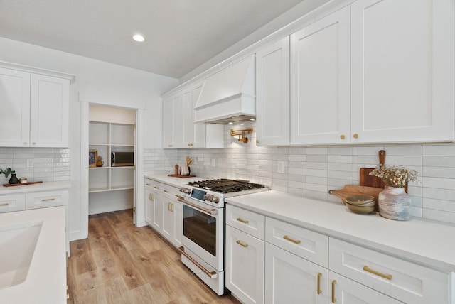 1217 E Granary Ct, Spokane, WA 99208 - kitchen featuring white gas range oven, custom exhaust hood, white cabinetry, decorative backsplash, and light countertops
