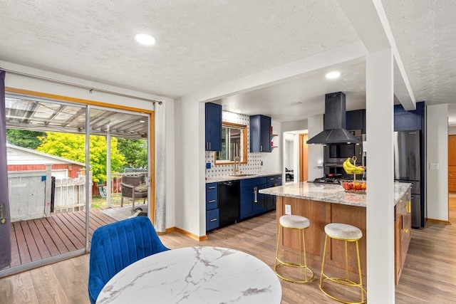 3225 E 16th Ave, Spokane, WA 99223 - kitchen featuring blue cabinetry, island exhaust hood, black dishwasher, a textured ceiling, and light wood-type flooring