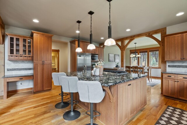 1122 E Hangman Ln, Spokane, WA 99224 - kitchen with built in appliances, light wood-type flooring, arched walkways, tasteful backsplash, and a breakfast bar area