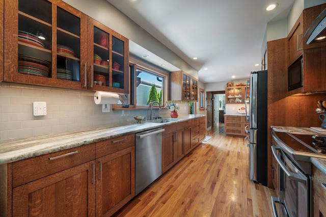 934 E 38th Ave, Spokane, WA 99203 - kitchen with stainless steel appliances, light wood finished floors, glass insert cabinets, tasteful backsplash, and brown cabinets