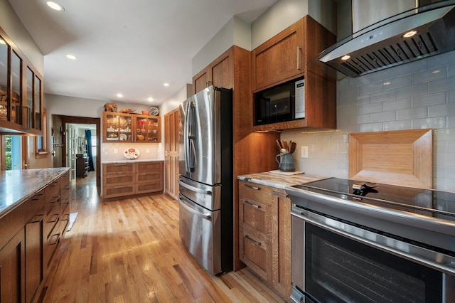 934 E 38th Ave, Spokane, WA 99203 - kitchen featuring appliances with stainless steel finishes, exhaust hood, brown cabinetry, light wood-style flooring, and glass insert cabinets