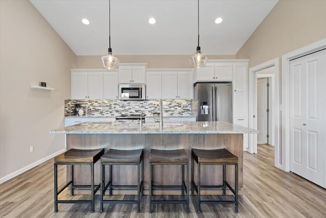 696 W Basalt Ridge Dr, Spokane, WA 99224 - kitchen featuring stainless steel appliances, white cabinets, backsplash, a center island with sink, and a kitchen breakfast bar