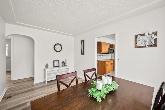 2603 E Wellesley Ave, Spokane, WA 99217 - dining area featuring arched walkways, a textured ceiling, light wood-style flooring, and baseboards