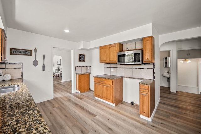 2603 E Wellesley Ave, Spokane, WA 99217 - kitchen featuring stainless steel microwave, arched walkways, decorative backsplash, dark stone counters, and light wood finished floors